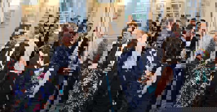 An event at BMA house. Men and women in semi-formal dress gather and talk with drinks in hand.