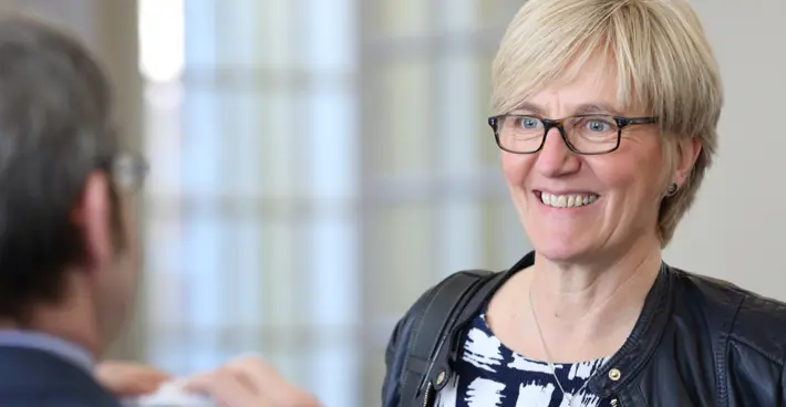A woman facing a man whose back is to camera and blurred. She seems to be smiling at something he is saying.