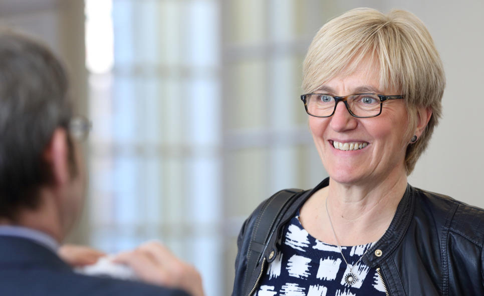 A woman facing a man whose back is to camera and blurred. She seems to be smiling at something he is saying.