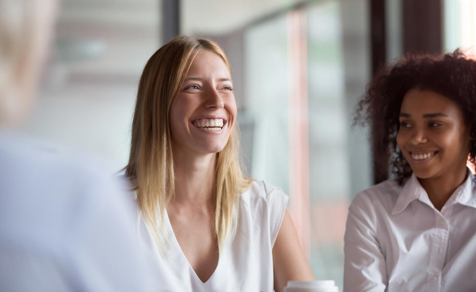 Two women in a group setting, one smiling and one laughing